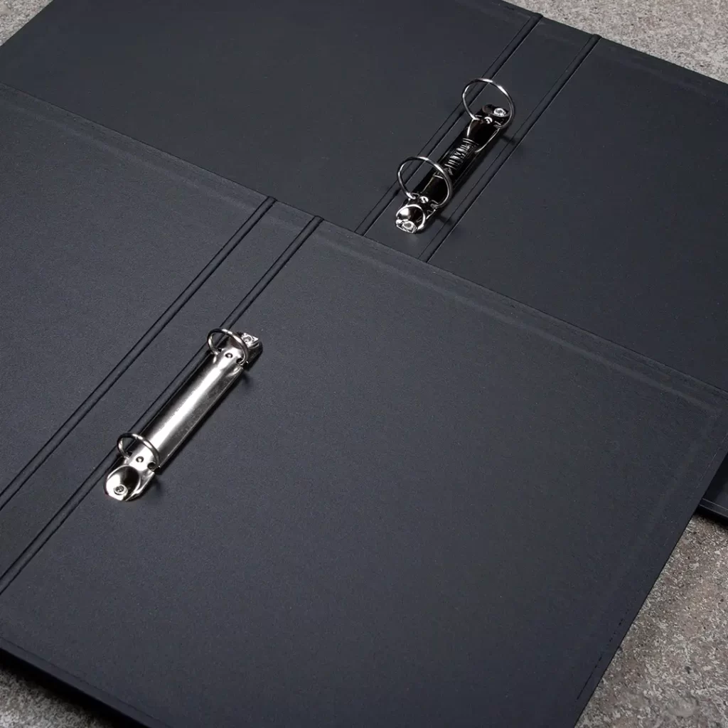 Kuorokansioiden mekanismeja. Erilaiset mekanismit, yhdessä mekanismi on kiinnitetty selkään ja toisessa takakanteen.